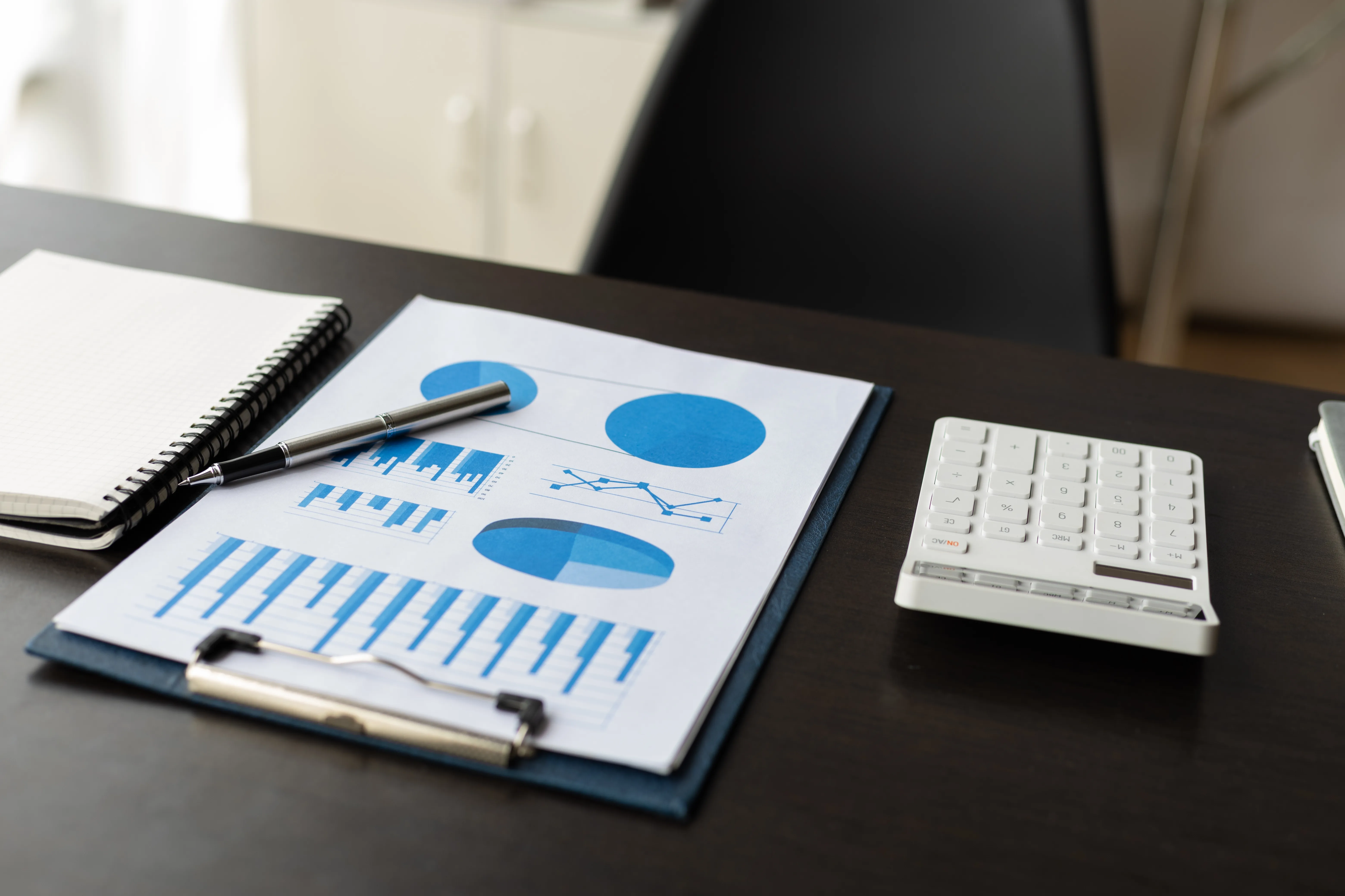 Financial charts on a clipboard beside a calculator and notebook on a desk.